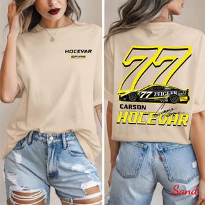 May include: Beige t-shirt with the text "HOCEVAR" and "SPARE" in black and yellow on the front. The back features a large yellow "77" with a race car graphic and the name "CARSON HOCEVAR" in yellow.