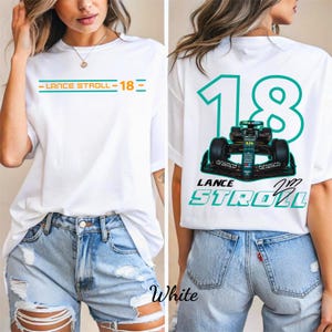 Op de afbeelding: Wit T-shirt met de tekst "LANCE STROLL - 18" in teal en oranje op de voorkant. De achterkant toont een teal "18" en een Formule 1-auto-afbeelding met de naam "LANCE STROLL".