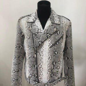 Może przedstawiać: Szara i biała skórzana kurtka ze wzorem skóry węża w klasycznym stylu motocyklowym. Kurtka posiada kołnierz z klapami, asymetryczne zapięcie na zamek i pasek w talii. Kurtka jest prezentowana na czarnym manekinie.