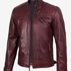 Puede incluir: Chaqueta de cuero burdeos con cuello alzado y cierre de cremallera frontal. La chaqueta presenta paneles acolchados en los hombros, dos bolsillos en el pecho con cremallera y dos bolsillos laterales. Las mangas tienen pu&ntilde;os con cremallera y correas ajustables en la cintura.