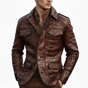 Könnte beinhalten: Braune Lederjacke mit Krokodilhautstruktur. Die Jacke hat einen Kragen, vier Vordertaschen und einen Knopfverschluss. Die Jacke wird über einem braunen Hemd getragen.