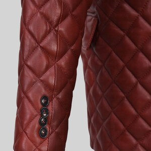 K&ouml;nnte beinhalten: Nahaufnahme einer burgunderfarbenen, gesteppten Lederjacke. Die Jacke hat ein Rautenmuster und drei dunkle Kn&ouml;pfe am &Auml;rmel. Das Design der Jacke deutet auf einen klassischen, ma&szlig;geschneiderten Stil hin.