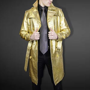 May include: A gold trench coat with a crocodile skin texture. The coat has a double-breasted design with large buttons, a belt, and a notched collar. The person is wearing a black shirt and a striped tie.
