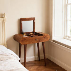 May include: A wooden vanity table with a flip-up mirror and storage compartments. The table has a curved design, a single drawer, and four tapered legs. The wood has a warm, reddish-brown tone, and the mirror is rectangular.