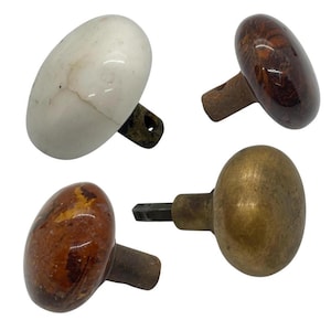May include: Four antique door knobs in various styles. One is white ceramic, one is dark wood, one is a lighter wood with a mottled pattern, and one is brass. Each knob has a different base and stem.