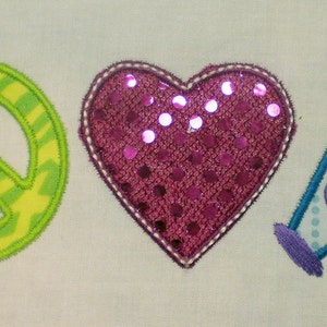 Puede incluir: Tres parches bordados: un signo de paz verde y amarillo, un corazón rosa con lentejuelas y un megáfono azul y morado con la palabra "Cheer" en él.