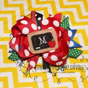 Peut inclure: Noeud en ruban à pois rouge, vert, bleu et jaune avec un tableau noir en feutre marron avec la lettre "M" et une pomme rouge. Le noeud est sur un fond jaune et blanc à chevrons.