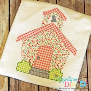 May include: A pink and white floral fabric applique of a schoolhouse with a bell on top, a gingham door, and green bushes. The applique is on a white fabric background. The text "The Applique Diva" is at the bottom of the image.