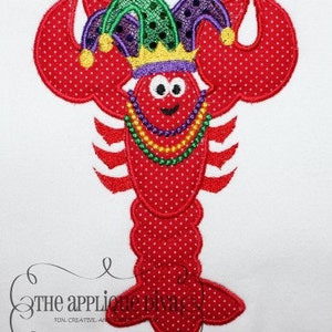 May include: Red embroidered lobster wearing a purple and green jester hat with a gold crown and a beaded necklace.