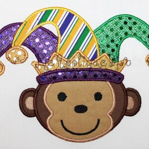 May include: Embroidered design of a monkey wearing a purple, green, and gold jester hat with sequins. The monkey has a brown face and a happy expression.