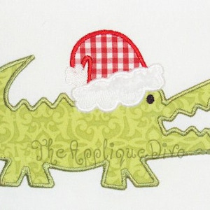 May include: A green alligator wearing a red and white checkered Santa hat with a white fur trim. The alligator has a wide open mouth with sharp teeth.