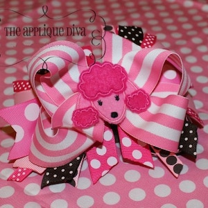 May include: Pink and white striped ribbon bow with a pink felt poodle applique. The bow is decorated with white polka dots and black polka dots.