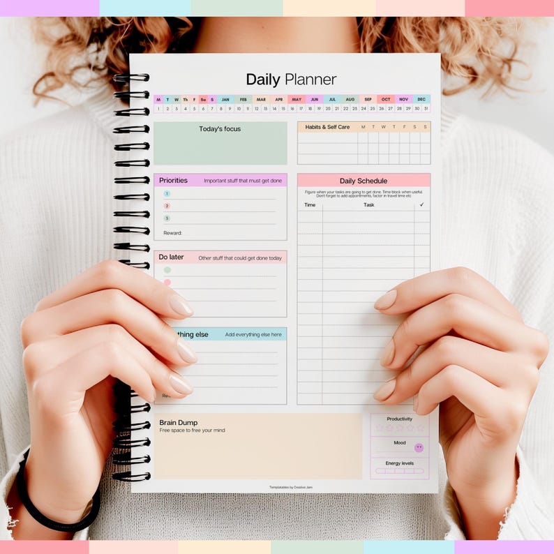 Puede incluir: Un cuaderno Daily Planner con encuadernaci&oacute;n en espiral negra. El planificador presenta secciones para horarios diarios, prioridades y un &aacute;rea de lluvia de ideas. El texto "Daily Planner" est&aacute; en la parte superior, con secciones como "Today's focus" y "Habits & Self Care".