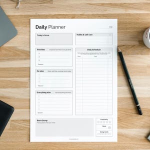 May include: A white daily planner sheet with sections for today's focus, priorities, and a daily schedule. A black pencil rests on the right side. The planner includes sections for habits, self-care, and a brain dump area.