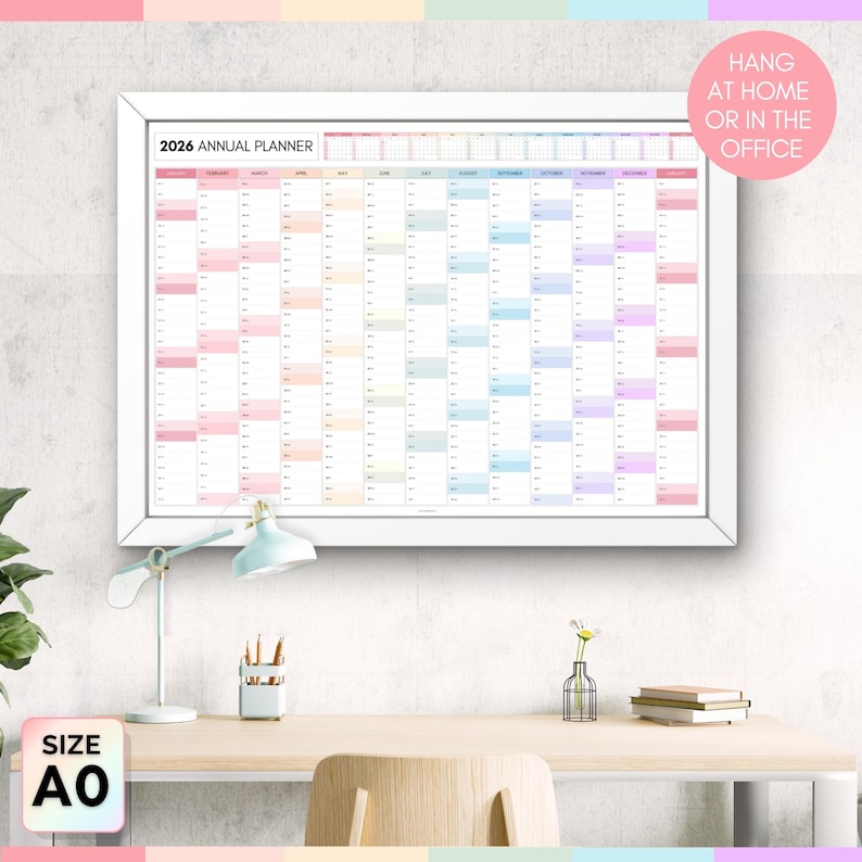 May include: A framed 2026 annual planner with a white border. The planner is filled with colorful blocks for each month and day. Text on the planner reads "2026 Annual Planner." Additional text in a pink circle says "Hang at home or in the office." The size is A0.