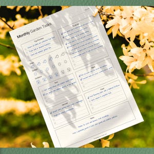 May include: A white printed Monthly Garden Tasks planner with sections for top priorities, to-do list, sunlight, fertilizers, sowing, harvest, plant, feed, and notes. The planner is clipped to a wooden surface with a gold clip, with a blurred floral background.