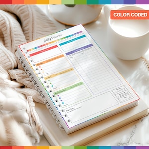 May include: A spiral-bound daily planner with a rainbow-coloured border and the words "Daily Planner" at the top. The planner includes sections for priorities, tasks, and a "Brain Dump" area. The text "Color Coded" is visible in the upper right corner.