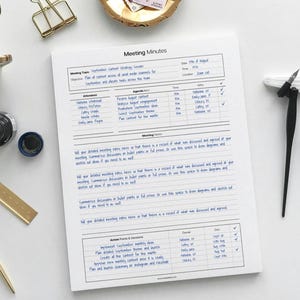 May include: A document titled "Meeting Minutes" with handwritten notes in blue ink. The paper includes sections for attendees, agenda, and action points. A gold-coloured paper clip and a pen are also visible.