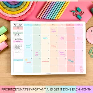 May include: A monthly planner with pastel-colored boxes for each day of the week. The planner includes a to-do list, notes section, and the text "PRIORITIZE WHAT'S IMPORTANT AND GET IT DONE EACH MONTH". Colored pencils and stationery are in the background.