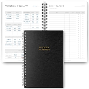 May include: A black Budget Planner notebook with a spiral binding, open to show financial planning pages. The cover has the words "BUDGET PLANNER" in gold lettering. The open pages display sections for monthly finances and bill tracking.