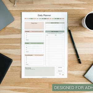May include: A white daily planner with sections for focus, priorities, and a daily schedule. The planner has a green and beige color scheme, with the text "Daily Planner" at the top. The bottom right corner reads "DESIGNED FOR ADHD".