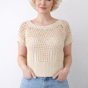 Peut inclure: Un haut en crochet crème à manches courtes avec un motif texturé. Le haut a un ourlet côtelé et une encolure dégagée. Le modèle porte un jean bleu clair. Le haut est un vêtement fait à la main.