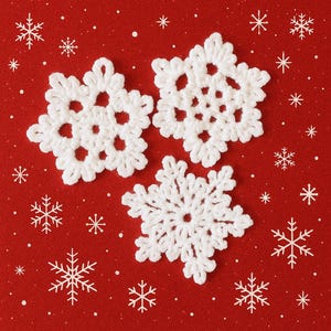 Peut inclure: Trois flocons de neige blancs crochetés sur un fond rouge avec des accents de flocons de neige et de points blancs. Les flocons de neige ont des motifs ajourés complexes, parfaits pour la décoration hivernale ou des fêtes.