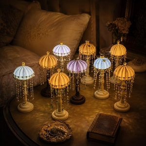 May include: A collection of eight small table lamps featuring sea urchin shell shades in white, yellow, and purple. Each lamp has a slender base and is adorned with hanging crystal bead strands that catch the warm, glowing light.
