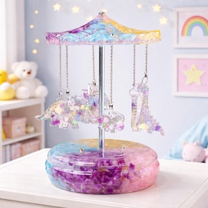 Może przedstawiać: Kolorowy, dekoracyjny przedmiot w stylu karuzeli z wielokolorową podstawą i przezroczystym wierzchem. Karuzela posiada wiszące ozdoby w kształcie dinozaurów i jest ozdobiona brokatem. Paleta kolorów obejmuje róż, fiolet, niebieski i żółty.