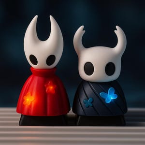 May include: Two stylized figurines with white heads and black eyes. One wears a red cape with glowing star accents, the other a navy blue cape with glowing butterfly accents. Both have black bases.