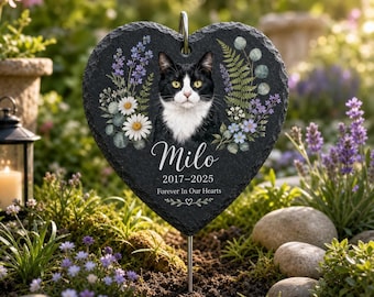 May include: A heart-shaped black slate memorial plaque featuring a portrait of a black and white cat surrounded by floral illustrations. The text reads Milo, 2017-2025, and Forever In Our Hearts, with a metal stake attached for garden display.