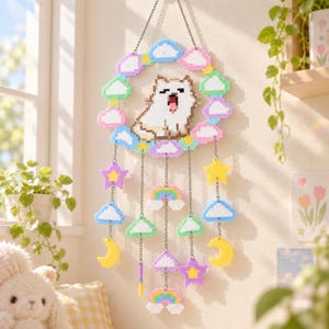 Peut inclure: Une décoration murale en perles à repasser représentant un chien blanc central entouré d'un cadre circulaire de nuages et d'étoiles pastel. Des chaînes pendent du cadre avec des perles en forme d'étoiles, de nuages, de lunes et d'arcs-en-ciel.