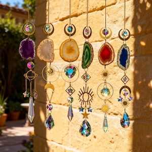 Può includere: Una collezione di acchiappasole sospesi con fette di agata in vari colori, tra cui viola, beige, arancione, verde, rosso e blu. Ogni acchiappasole presenta dettagli in metallo dorato, cristalli e ciondoli a tema celeste come lune, stelle e soli.