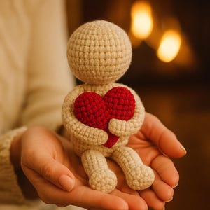 Könnte beinhalten: Eine beige gehäkelte Figur, die ein rotes Herz hält. Die Figur hat einen runden Kopf, Arme und Beine. Der Text auf dem Bild lautet: "When words aren't enough... gift a heartbeat woven with love."