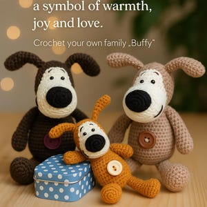 May include: Three crocheted dog toys in shades of brown and orange, with white and black details. The dogs have button eyes and noses. A blue tin with white polka dots is in front. Text reads: "a symbol of warmth, joy and love. Crochet your own family, Buffy."