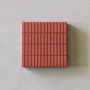 Puede incluir: Un azulejo cuadrado de color terracota que presenta un patrón repetitivo de hendiduras rectangulares verticales dispuestas en cuadrícula. La superficie es mate y uniforme, mostrando un diseño estructurado con líneas limpias y un espaciado constante.