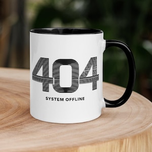 May include: A white ceramic mug with a black interior and a black handle. The front of the mug features the text 404 in a large, bold, horizontally striped font, with the words SYSTEM OFFLINE printed in a smaller, solid black sans-serif font below.