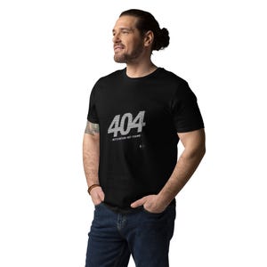 Könnte beinhalten: Ein schwarzes kurzärmeliges T-Shirt mit dem weißen Text 404 und dem Schriftzug MOTIVATION NOT FOUND auf der Brust. Das Design enthält eine kleine kreisförmige Grafik unter dem Text. Das T-Shirt hat einen Rundhalsausschnitt und eine Standardpassform.