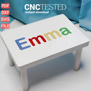 Op de afbeelding: Een witte houten kindertafel met de naam "Emma" in kleurrijke letters. De tafel heeft vier poten en de tekst "CNC TESTED" en "Instant download" zijn zichtbaar.