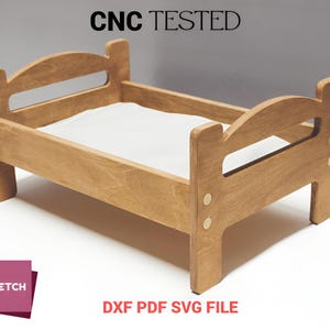 Peut inclure: Un petit lit en bois pour poupée, de couleur marron clair. Le lit a un cadre rectangulaire avec une tête et un pied de lit, et un matelas blanc. Le texte "CNC TESTED" est au-dessus du lit. Le texte "DXF PDF SVG FILE" est en dessous.