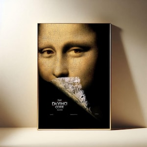 May include: A framed poster featuring a close-up of the Mona Lisa's face with a portion of a document covering her mouth. The poster has a gold frame and the title "The Da Vinci Code" is displayed in white text.