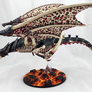 May include: A detailed miniature model of a winged creature with a black and bone-colored body, red accents, and wings patterned with brown and red spots. The model is mounted on a base depicting a fiery, lava-like surface.