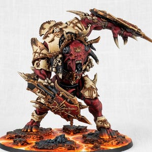 May include: A detailed miniature figure of a demonic creature with red skin, horns, and sharp teeth. It is clad in ornate, bone-colored armor and wields two large, spiked shields. The figure stands on a base depicting a fiery landscape.