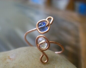May include: A copper wire ring with a blue and clear glass bead. The ring is made of copper wire and has a simple design.