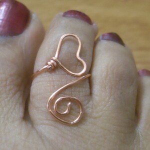 May include: A copper wire toe ring with a heart design. The ring is worn on the big toe of a foot.