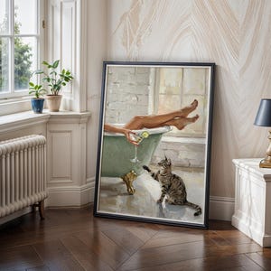 Op de afbeelding: Een ingelijst schilderij toont een persoon in een mintgroene badkuip met een cocktail en een kat. Het kunstwerk wordt tentoongesteld in een kamer met een raam, planten en een lamp.