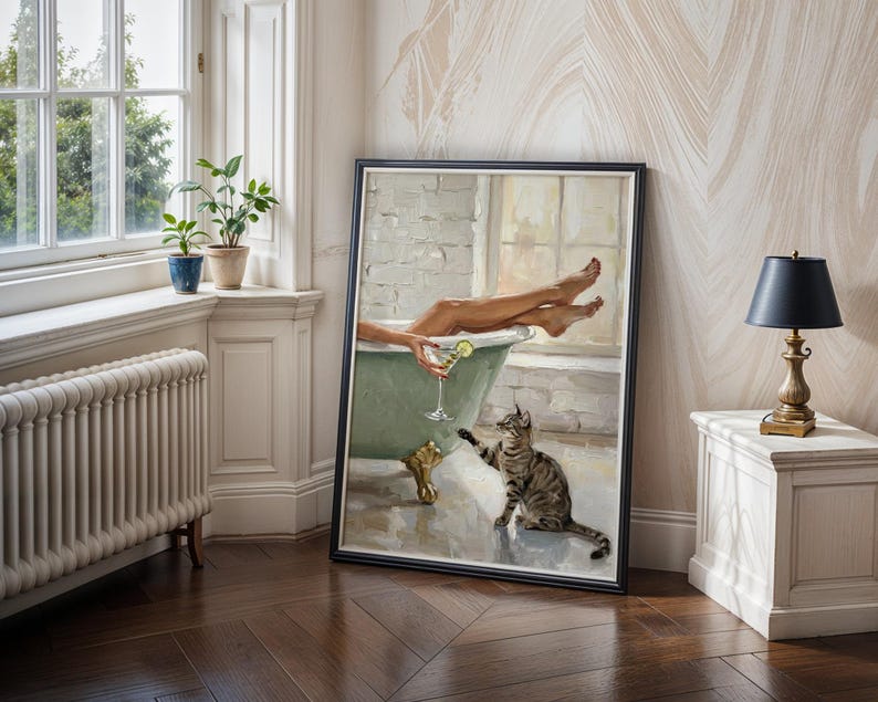 Op de afbeelding: Een ingelijst schilderij toont een persoon in een mintgroene badkuip met een cocktail en een kat. Het kunstwerk wordt tentoongesteld in een kamer met een raam, planten en een lamp.