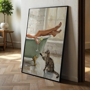 Op de afbeelding: Een ingelijste kunstdruk toont een ontspannende sc&egrave;ne. Een persoon zit in een groene badkuip met een cocktail, en een gestreepte kat reikt ernaar. Het kunstwerk heeft een vintage esthetiek, met zachte kleuren en een focus op ontspanning.
