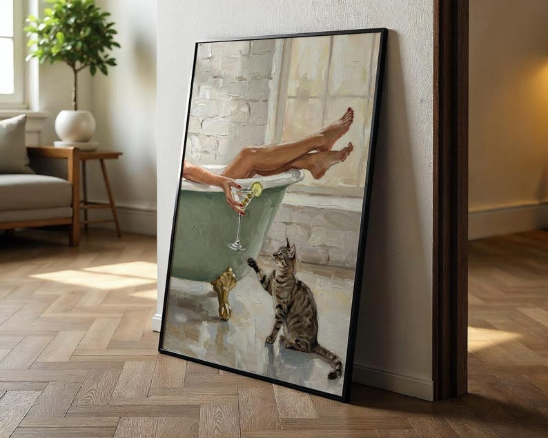 Op de afbeelding: Een ingelijste kunstdruk toont een ontspannende sc&egrave;ne. Een persoon zit in een groene badkuip met een cocktail, en een gestreepte kat reikt ernaar. Het kunstwerk heeft een vintage esthetiek, met zachte kleuren en een focus op ontspanning.