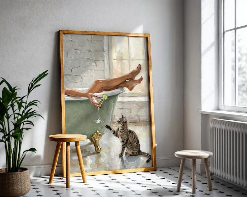 Op de afbeelding: Een ingelijst schilderij toont een ontspannende sc&egrave;ne in een badkamer. Een persoon zit in een groene badkuip en houdt een cocktail vast. Een gestreepte kat reikt naar het drankje. Het schilderij staat in een kamer met een plant en twee houten krukken.